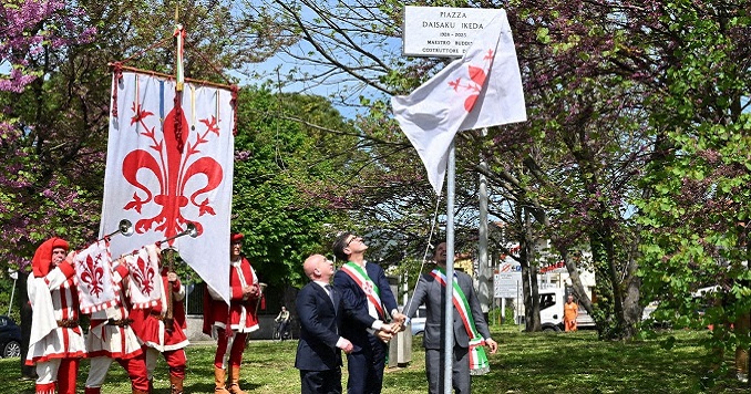 三個人正揭開牌匾，後方有四名號角樂隊的成員和佛羅倫薩旗幟。