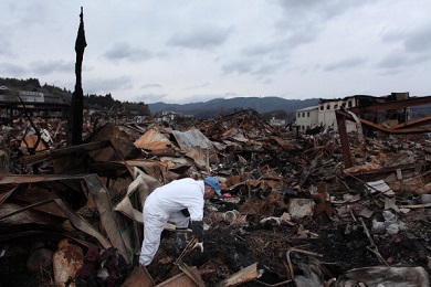 A man stands amidst a vast expanse of wreckage in a flattened landscape.