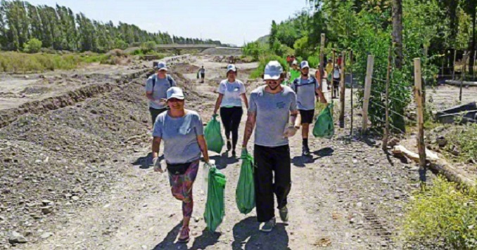 Un grupo de jóvenes con bolsas de residuos caminan por un sendero de montaña.