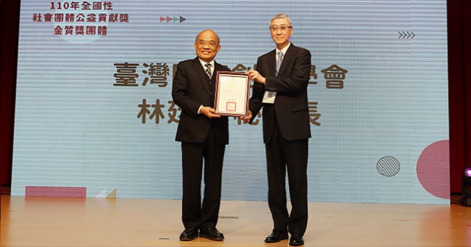 Dos hombres de pie en una tarima muestran un certificado