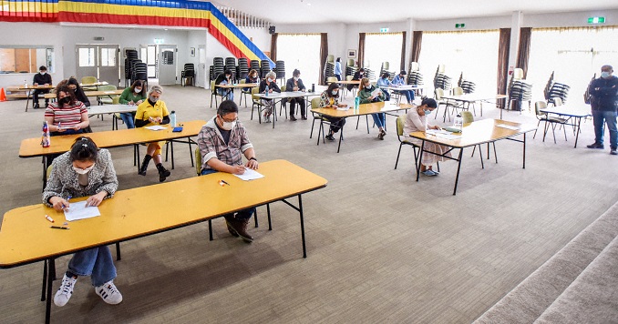 People seated in a large hall taking an exam