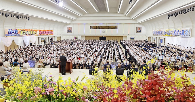 People seated in a grand hall facing a stage.