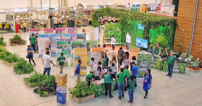 People walking through an exhibition in an event hall with plants and book fair booths.