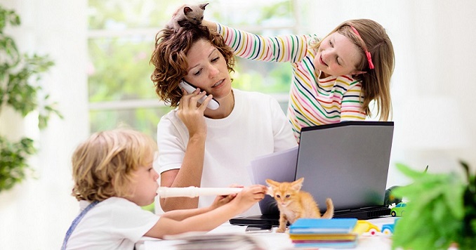 Imagen de archivo de una mujer que intenta trabajar en su ordenador mientras dos niños pequeños la distraen.