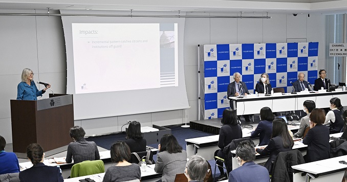 People in a conference room facing the front listening to a speaker standing at a podium.