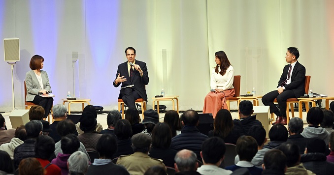 Four people sitting on a stage in front of an audience.