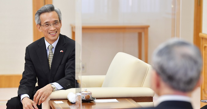 A smiling seated man in conversation with another man