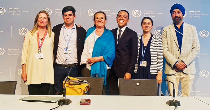 Foto de grupo de seis personas de pie en un escenario con logotipos de la ONU sobre el cambio climático como telón de fondo.