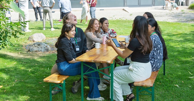 Students seated around a table outdoors chatting.