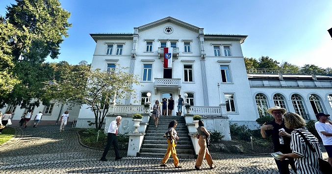 Un edificio blanco bajo el cielo azul y gente paseando fuera del edificio.