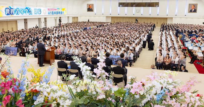 广大会场坐满人，照片的前景是陈列的鲜花。