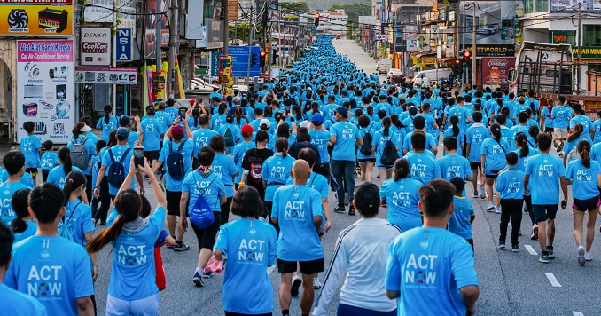 Miles de corredores con camiseta azul y el lema «Actúa ahora» del evento Corre por la paz llenan una calle.