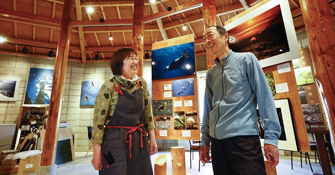 Two people standing next to each other smiling against a backdrop of a photo display in a museum