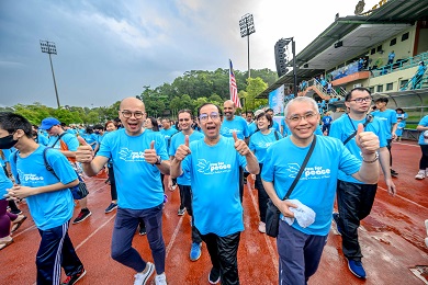 Un grupo de hombres con camisetas azules de «Actúa Ahora» en una pista de atletismo sonríen y hacen una señal con el pulgar hacia arriba