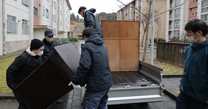 Un grupo de personas cargan en un auto los muebles dañados. 