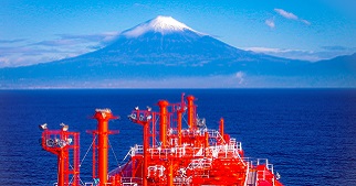 Large red vessel in the ocean with a view of a snow-capped mountain in the background.