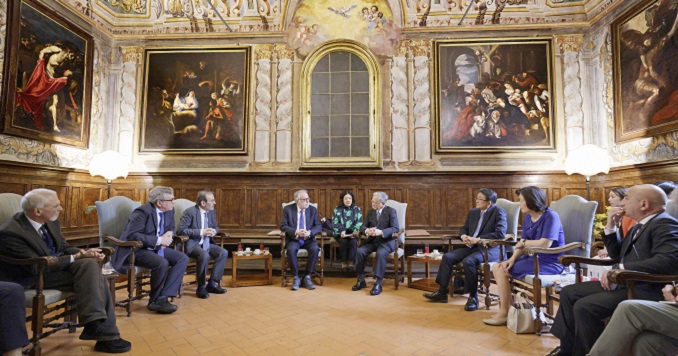 People seated in a circle, conversing in a hall with paintings.