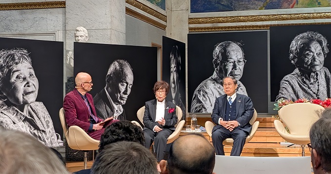 讨论会的3名讲者坐在原爆幸存者的巨大相片前方。