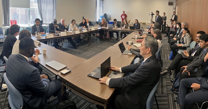 Diverse people, formally dressed, sitting around tables in a rectangular formation.