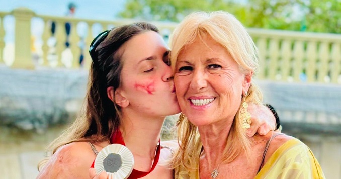 A young woman with a silver medal kissing her mother.