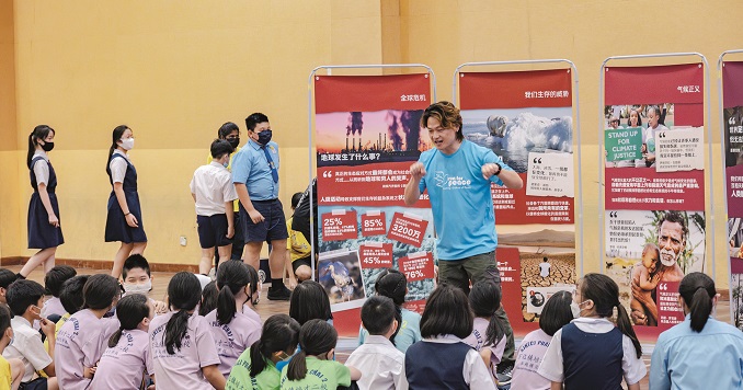 A man standing in front of exhibition panels that promote the SDGs talking to school children.