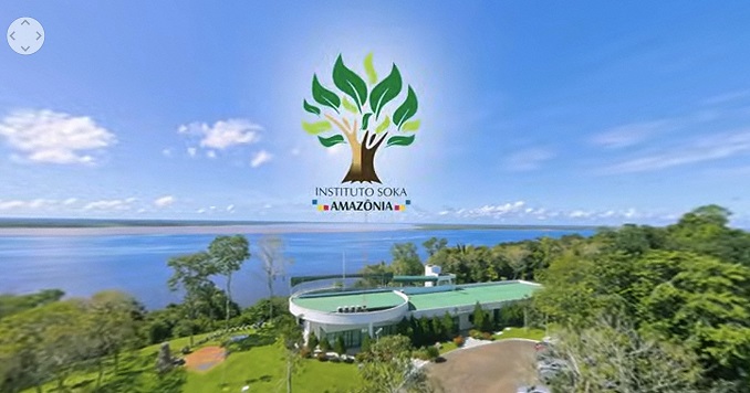 An aerial view of a building next to a river with green grass and trees around it.