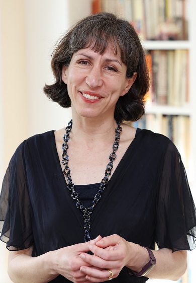 A woman dressed elegantly in black smiles at the camera, with a bookcase in the background