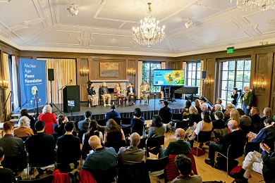 Four panelists talk on stage while participants listen in a wood-paneled room with a chandelier.