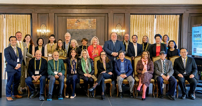 Formally dressed individuals from diverse backgrounds seated on antique chairs in front of a wood-paneled wall.