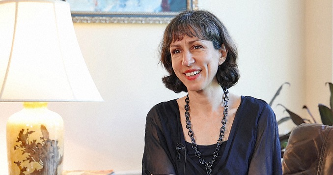 A woman dressed elegantly in black, sitting next to an ornate lamp.