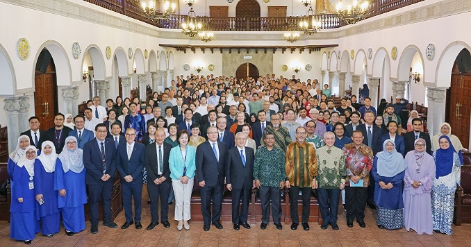 People standing in a large hall with a gallery and smiling for a commemorative photo.
