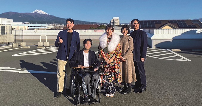 A family gathers for a photo with a relative in a wheelchair, with Mount Fuji visible behind them.