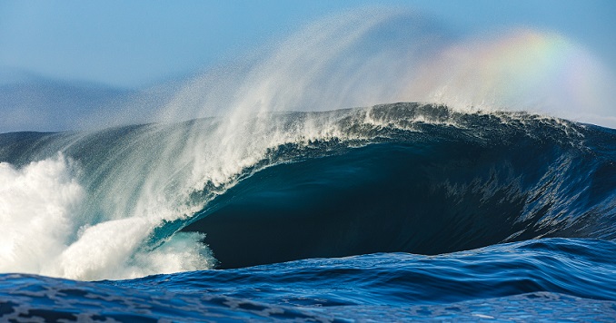 A powerful wave with a rainbow reflected in the spray.