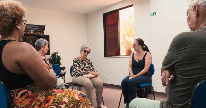 Several people sitting on chairs in a small room having a discussion.