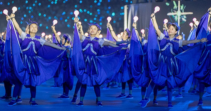Young dancers in flowing purple dresses hold up lights against a starlit background.