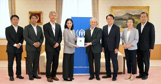 Eight people standing in a line for a commemorative photo at a donation ceremony.