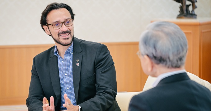 A man with glasses and a beard speaking animatedly to another person.