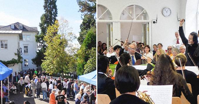 An orchestra performs under the direction of a conductor (left) and people in conversation outside Villa Sachsen, a white building.