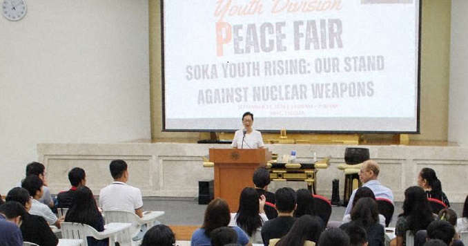 A speaker at a podium addressing an audience in a large conference hall.