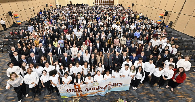 Large group of people in a hall with a commemorative banner.