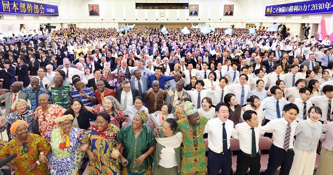 A large hall full of people standing, linking arm in arm.