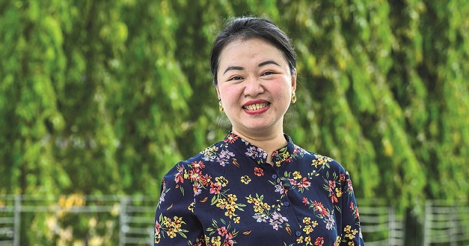 Photo of a woman smiling against a backdrop of green trees