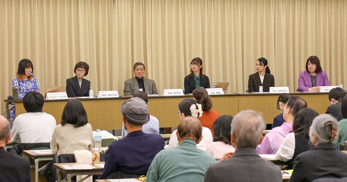 People sitting at a long desk with a name placards in front of them.