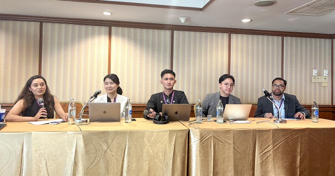 A panel of five young people seated behind desks.