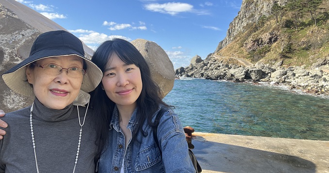An older woman and her daughter stand in front of a beautiful beach.