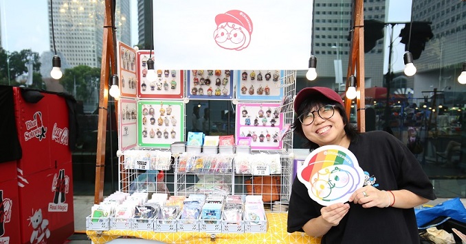 A woman standing in front of an art booth displaying her illustrations