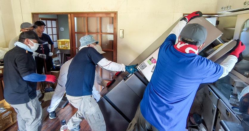 A group of men removing a refrigerator from a room damaged in the 2026 Kumamoto Earthquake.