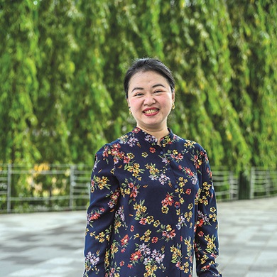 Szi Hean, sonriente ante un fondo de vegetación, lleva una prenda morada con estampado floral.