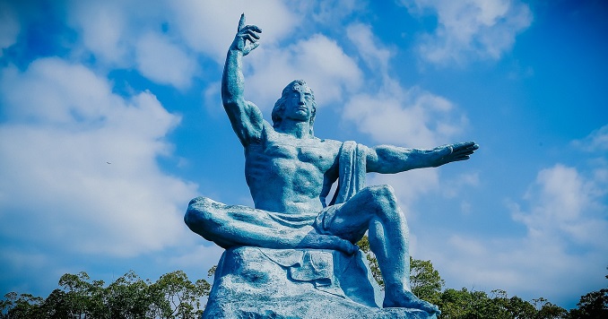 Statue of sitting man with right arm in air and left arm pointing