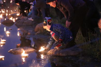 Una mujer y un niño hacen flotar una vela desde la orilla del lago durante la noche